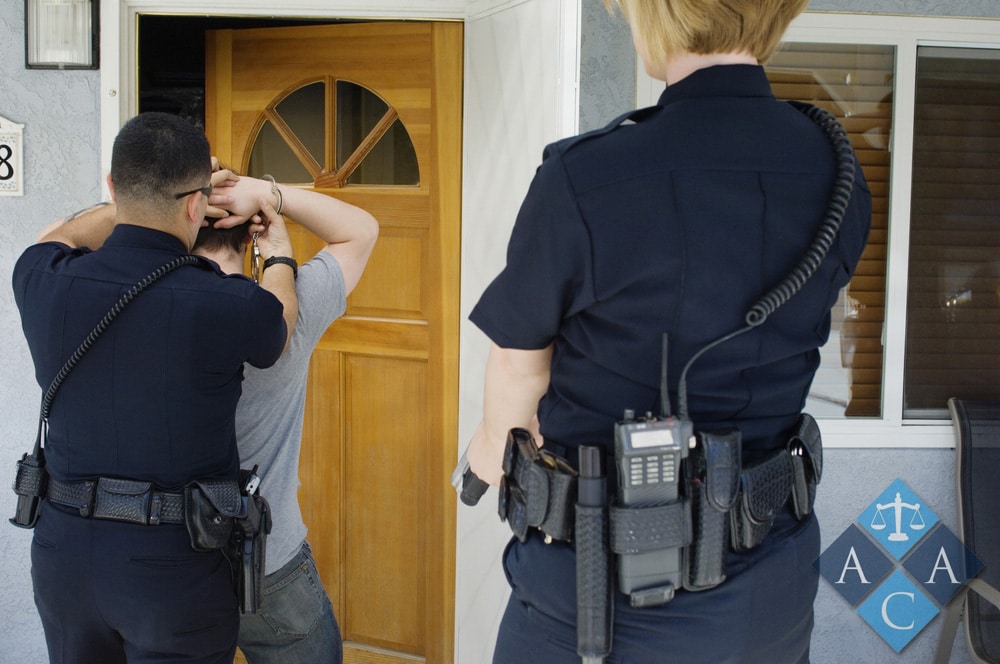 Rear view of police officers arresting young man with house in the background