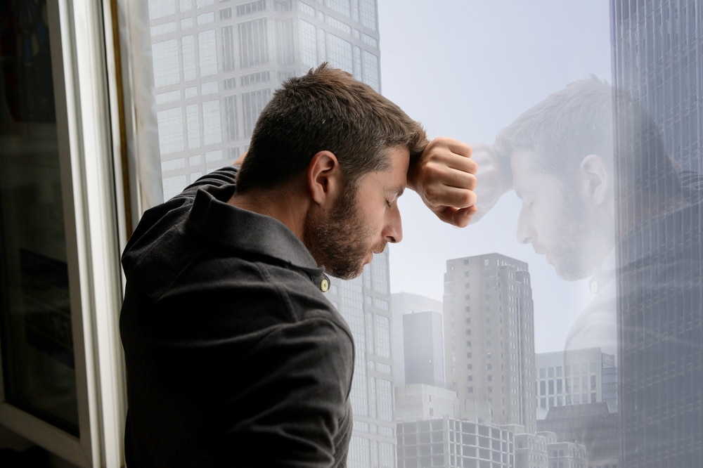 attractive man leaning on business district window suffering emotional crisis and depression