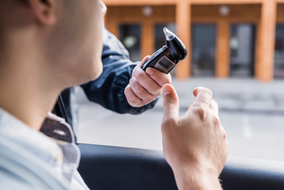 cropped view of policeman giving breathalyzer to driver in car, blurred foreground