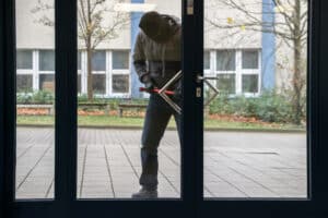 Hooded Man Using Crowbar To Open Glass Door